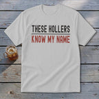 White t-shirt with "THESE HOLLERS KNOW MY NAME" printed in black and red.