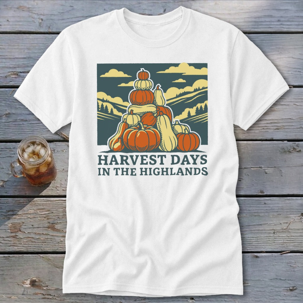 A white t-shirt featuring a retro graphic of stacked pumpkins, mountains, and the text Harvest Days in the Highlands.