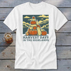 A white t-shirt featuring a retro graphic of stacked pumpkins, mountains, and the text Harvest Days in the Highlands.