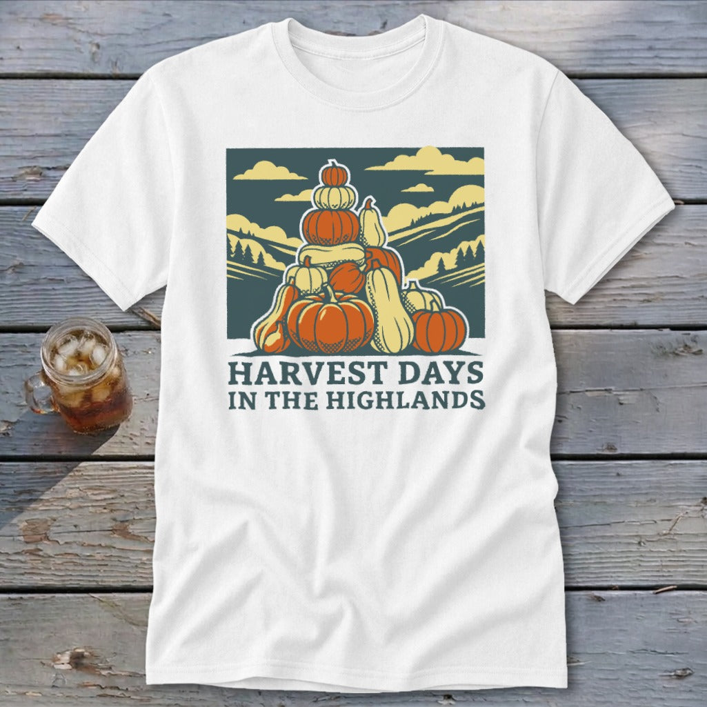 A white t-shirt featuring a retro graphic of stacked pumpkins, mountains, and the text Harvest Days in the Highlands.