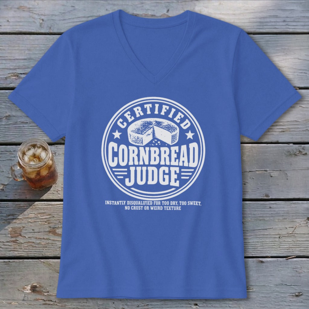 A blue V-neck t-shirt with a white graphic reading Certified Cornbread Judge laid flat on weathered wood.