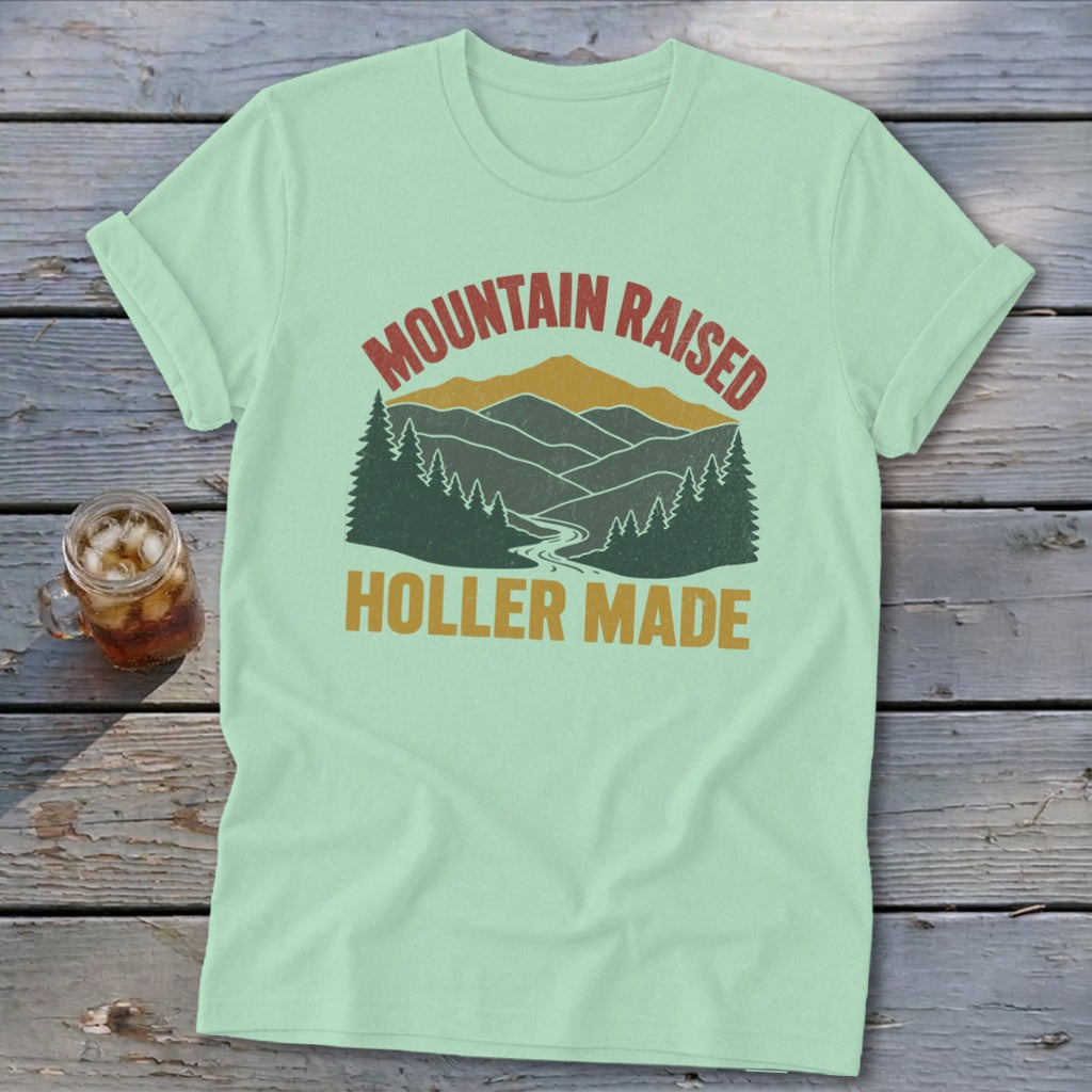 A mint green t-shirt featuring a retro mountain landscape graphic with the text Mountain Raised Holler Made.