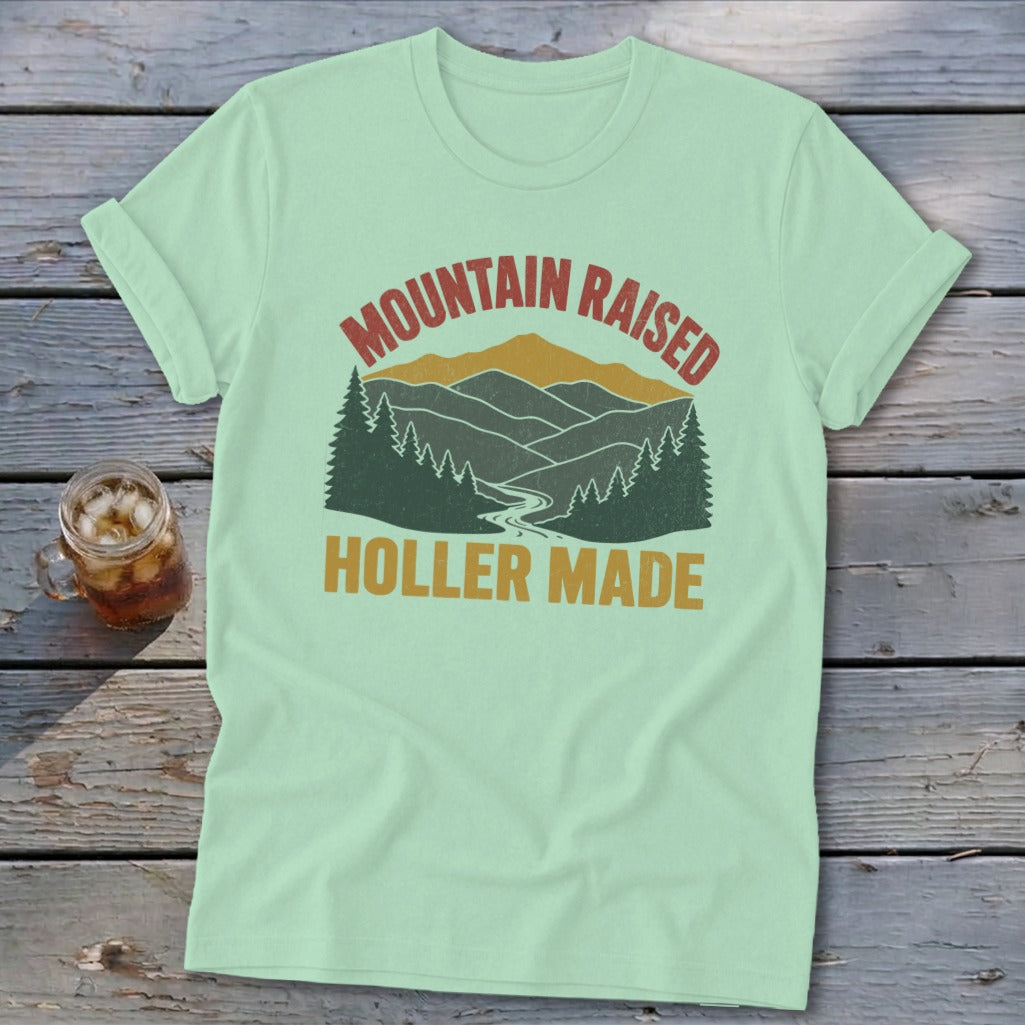 A mint green t-shirt featuring a retro mountain landscape graphic with the text Mountain Raised Holler Made.