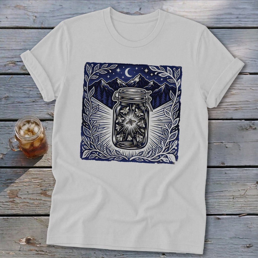 White t-shirt with a dark blue graphic of fireflies in a jar under a starry night sky.