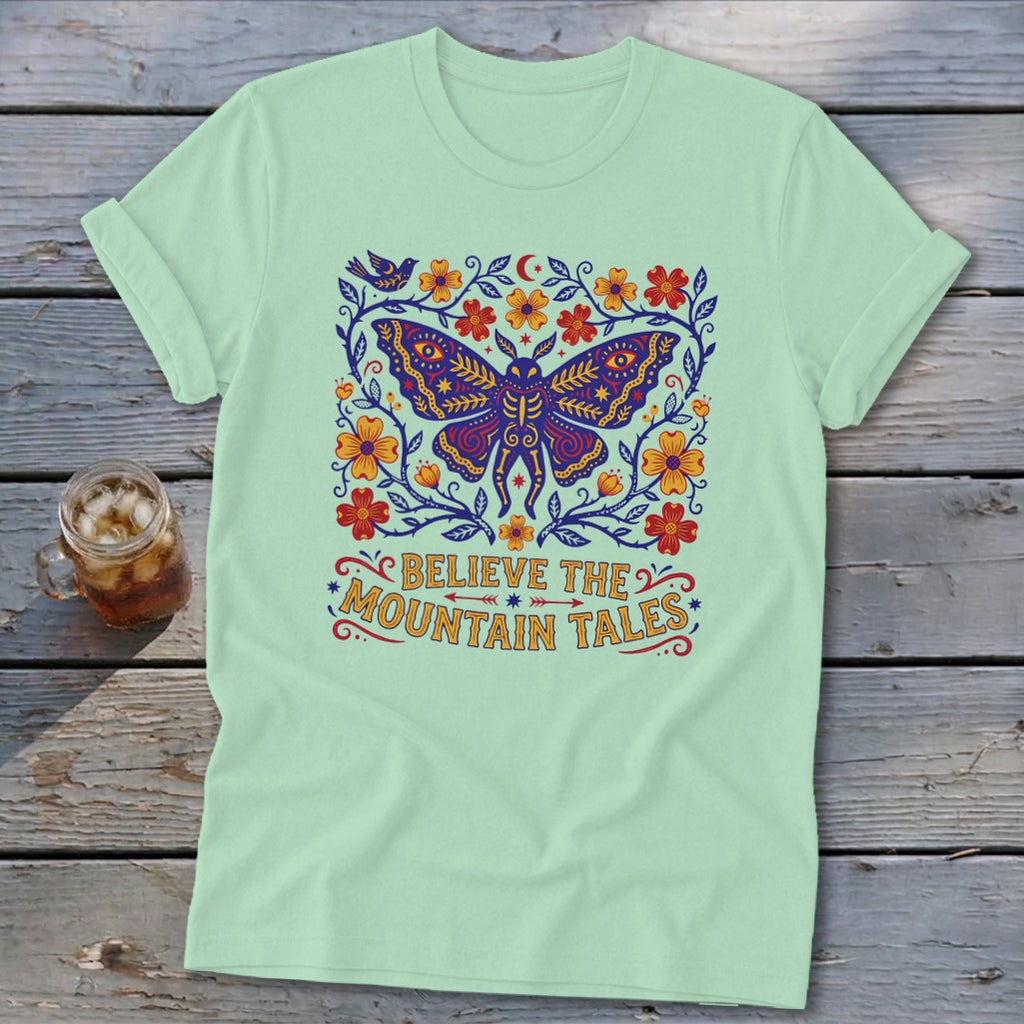 Mint t-shirt with a large colorful moth, flowers, and the text "BELIEVE THE MOUNTAIN TALES."