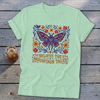 Mint t-shirt with a large colorful moth, flowers, and the text "BELIEVE THE MOUNTAIN TALES."