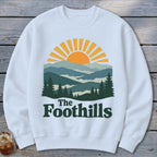 White sweatshirt with "The Foothills" text and a mountain landscape graphic.