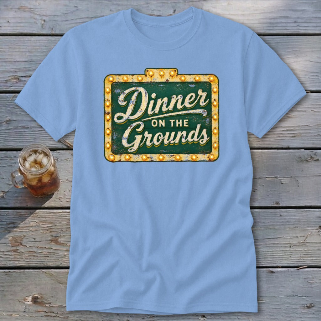 A light blue t-shirt featuring a green sign graphic that reads Dinner on the Grounds.