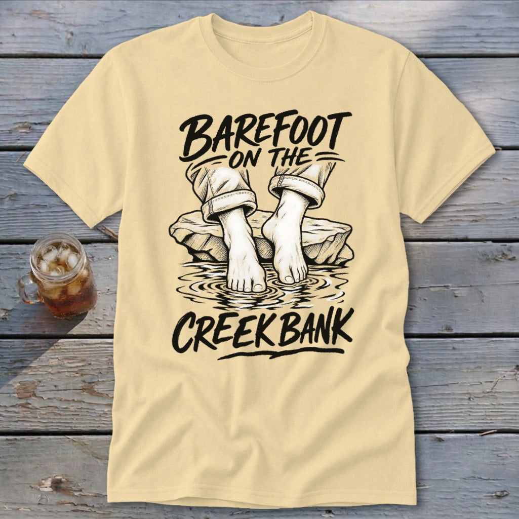 Light yellow t-shirt with "Barefoot on the Creek Bank" text and illustration of feet in water.