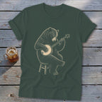 Bear playing a banjo on a stool, graphic on a dark green t-shirt.