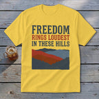 Yellow t-shirt with the text FREEDOM RINGS LOUDEST IN THESE HILLS above a retro mountain graphic.
