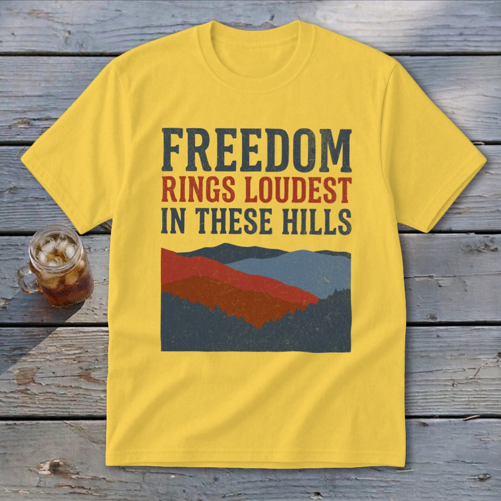 Yellow t-shirt with the text FREEDOM RINGS LOUDEST IN THESE HILLS above a retro mountain graphic.