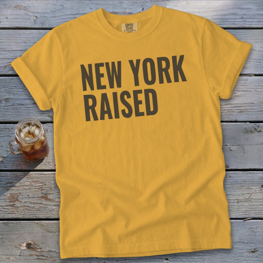 Yellow t-shirt with "NEW YORK RAISED" text on a wooden background.