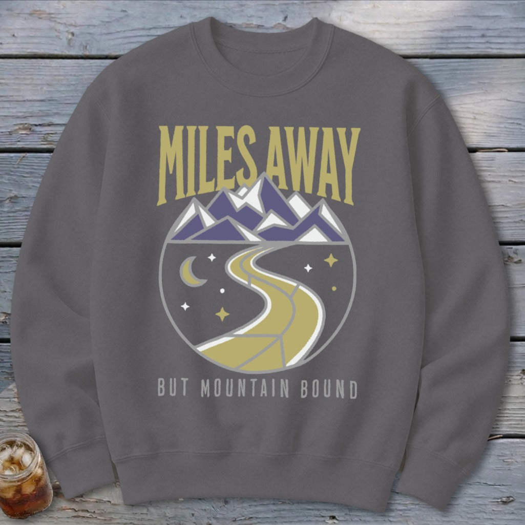 Grey sweatshirt with "MILES AWAY BUT MOUNTAIN BOUND" text and mountain landscape graphic.