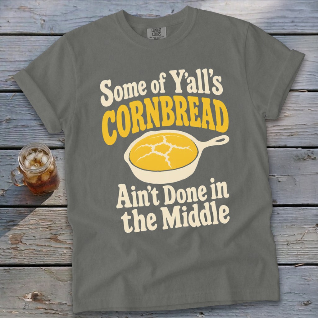 A gray t-shirt featuring the text Some of Y’all’s Cornbread Ain’t Done in the Middle with a cornbread illustration.