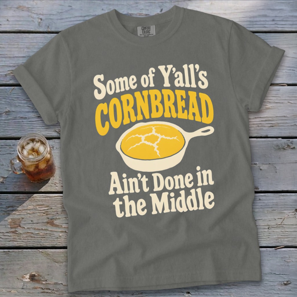 A gray t-shirt featuring the text Some of Y’all’s Cornbread Ain’t Done in the Middle with a cornbread illustration.