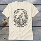 A cream t-shirt with a black line art graphic of a whippoorwill, corn stalks, and text.