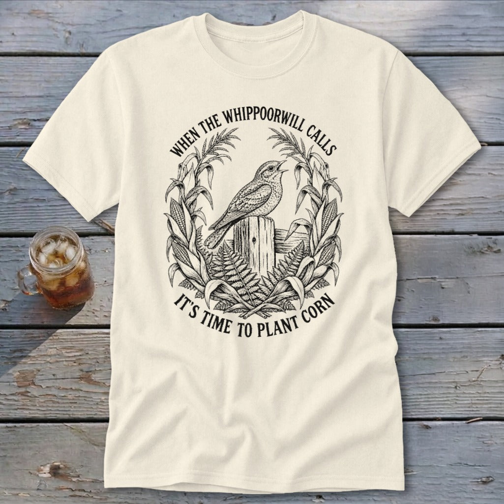 A cream t-shirt with a black line art graphic of a whippoorwill, corn stalks, and text.