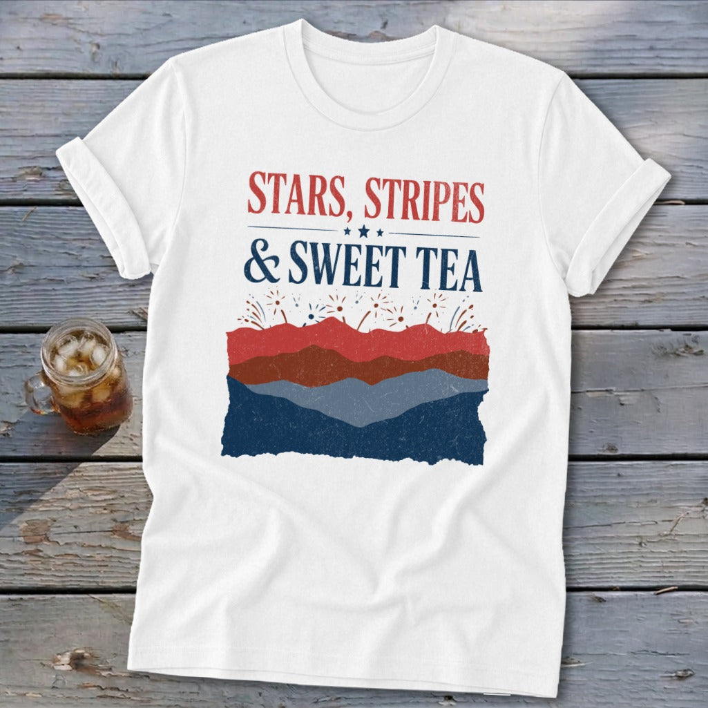 A white t-shirt with rolled sleeves features red, white, and blue text reading "STARS, STRIPES & SWEET TEA" above a landscape design of layered hills and fireworks.