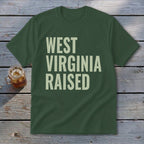 Green t-shirt with "WEST VIRGINIA RAISED" text in cream letters.