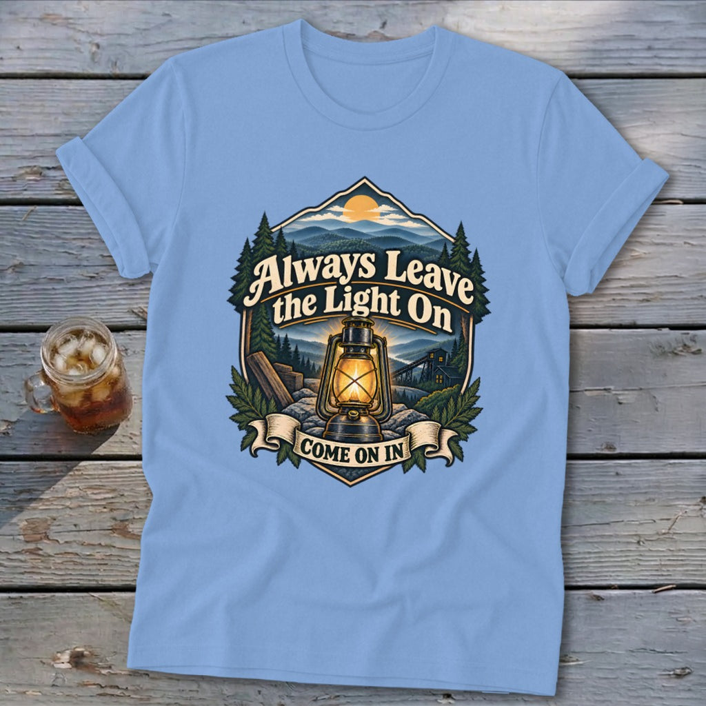Light blue t-shirt with a graphic of a lantern and mountains, saying "Always Leave the Light On. Come On In."