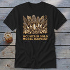 Black t-shirt with a golden illustration of morel mushrooms, ferns, and acorns. Text reads "Mountain Gold Morel Harvest".