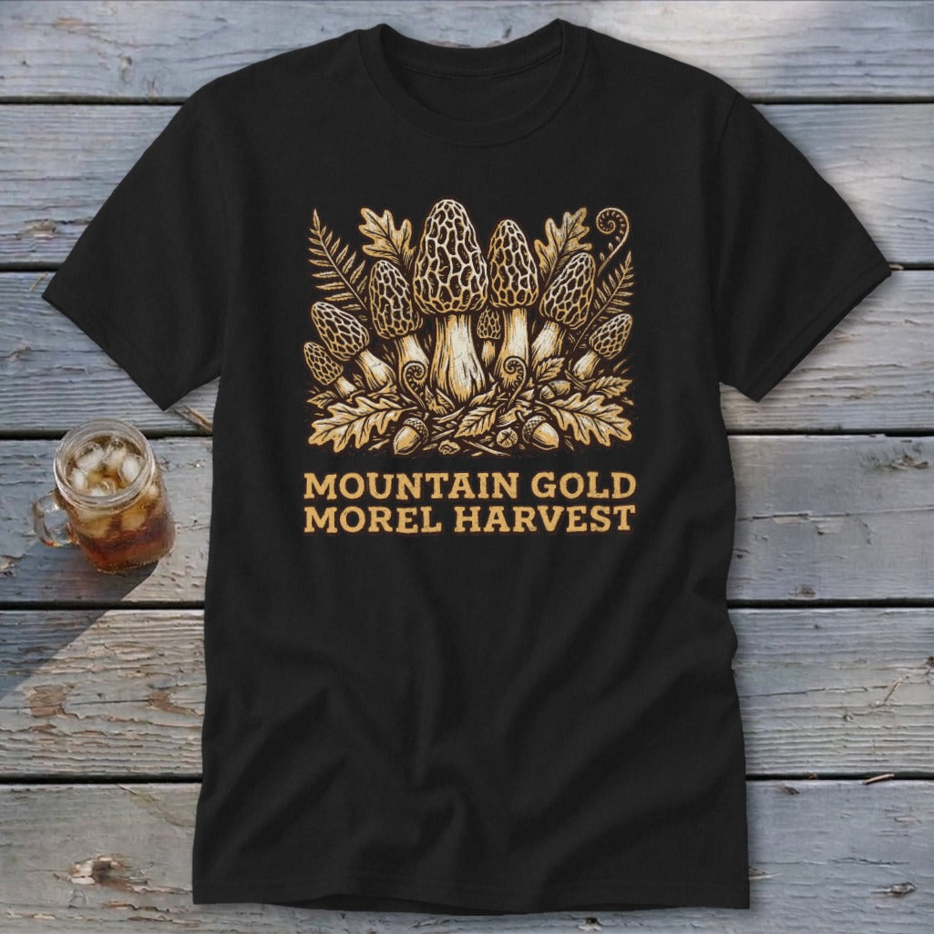 Black t-shirt with a golden illustration of morel mushrooms, ferns, and acorns. Text reads "Mountain Gold Morel Harvest".
