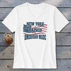 White V-neck t-shirt featuring a distressed American flag graphic with the text New York Raised American Made.