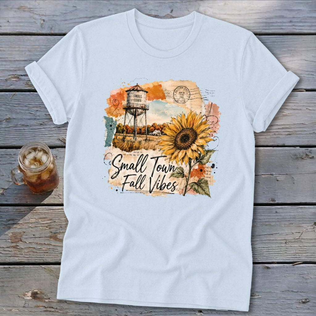 Light blue t-shirt with a graphic featuring a water tower, sunflower, and text "Small Town Fall Vibes."