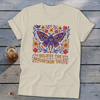 Cream t-shirt with a large purple moth surrounded by flowers and the text "BELIEVE THE MOUNTAIN TALES".