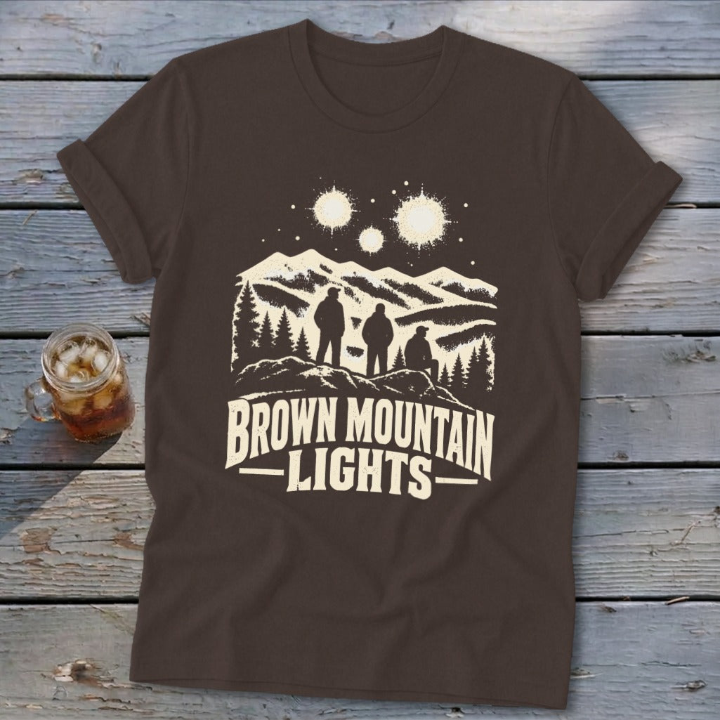 A brown short-sleeve t-shirt with a graphic of three figures, mountains, and glowing lights.