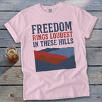 Light pink t-shirt with "Freedom Rings Loudest In These Hills" text over mountainous landscape.