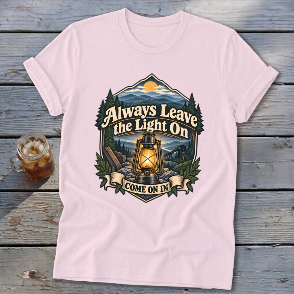 Light pink t-shirt with a graphic of a lantern and mountains, reading "Always Leave the Light On Come On In".