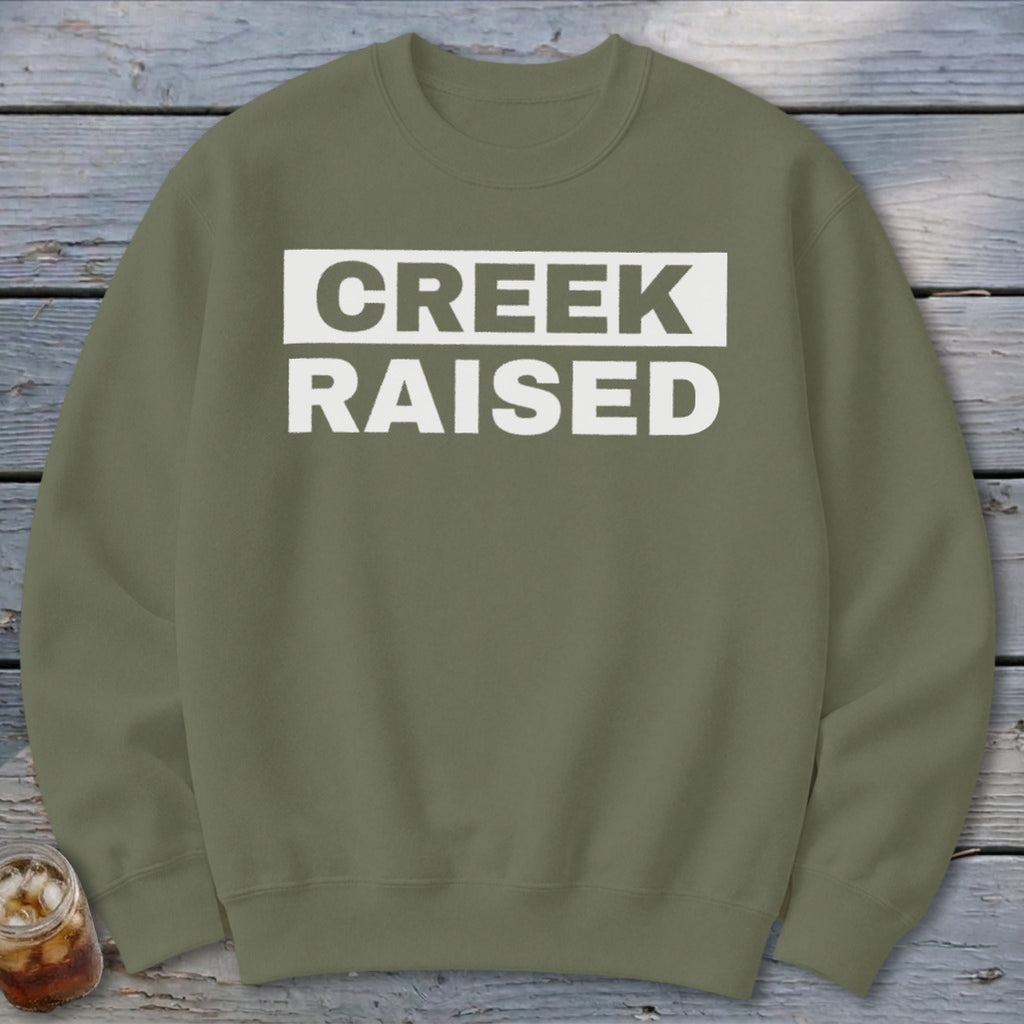 Olive green sweatshirt with white text reading "CREEK RAISED"