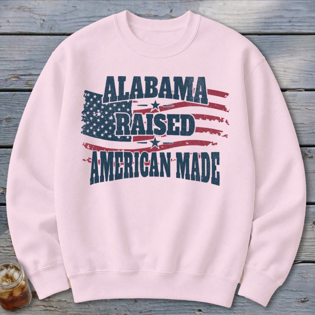 Light pink sweatshirt with distressed American flag graphic and text "Alabama Raised American Made".