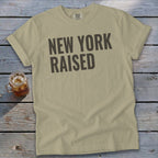 Tan t-shirt with dark gray "NEW YORK RAISED" text and a glass of iced tea.