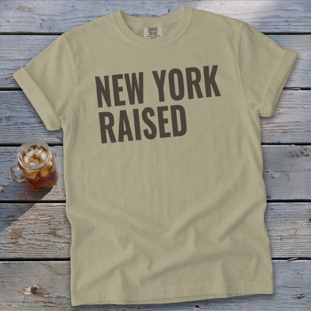 Tan t-shirt with dark gray "NEW YORK RAISED" text and a glass of iced tea.