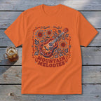 Orange t-shirt featuring a folk-style illustration of an acoustic guitar, sunflowers, leaves, and the text MOUNTAIN MELODIES.