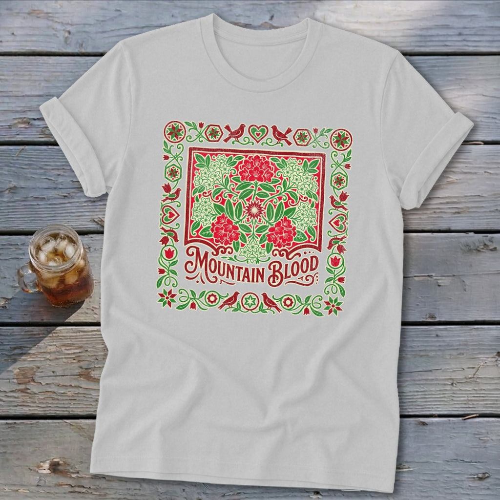 White t-shirt with red and green floral design and "MOUNTAIN BLOOD" text.