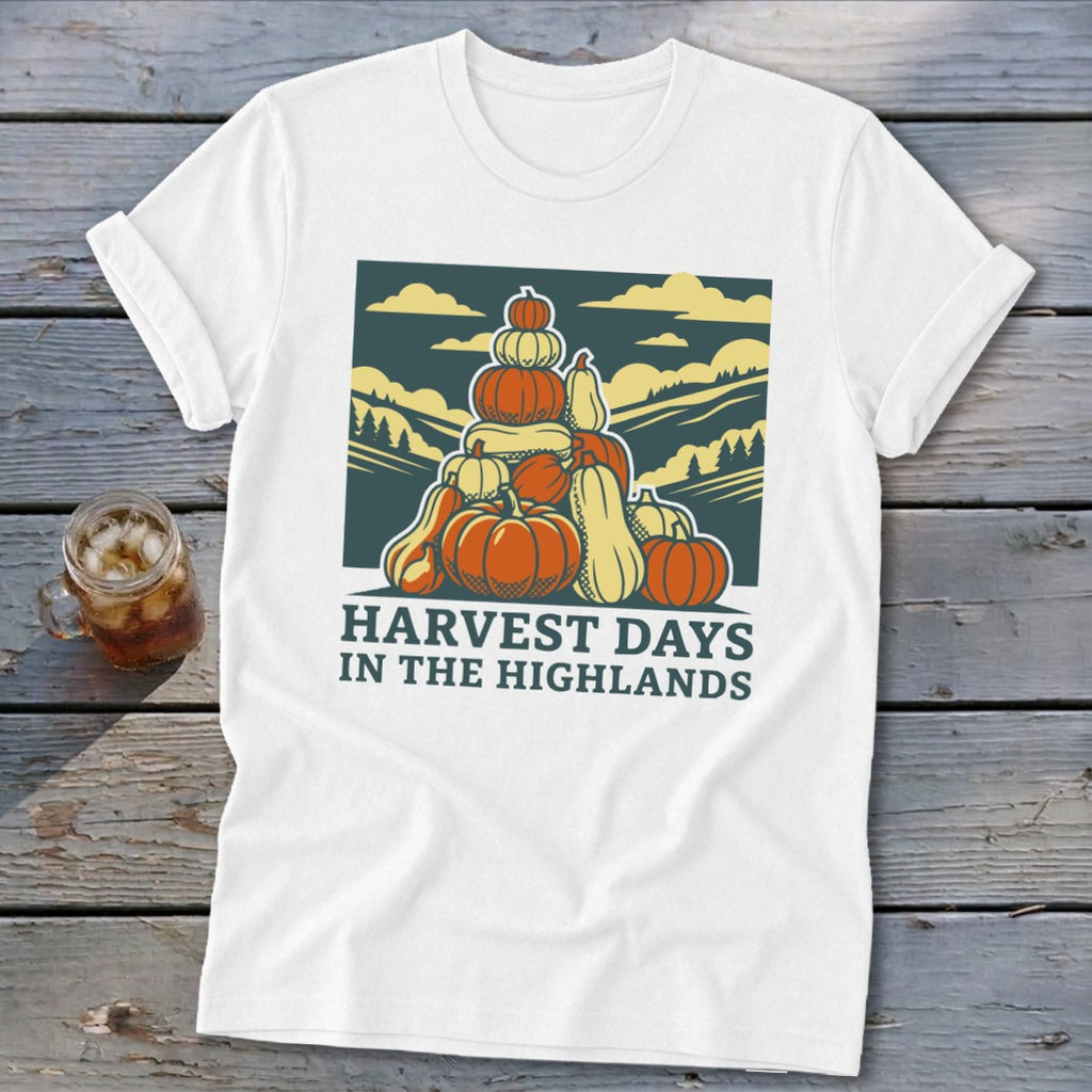 A white t-shirt featuring a graphic of stacked pumpkins, rolling hills, and the text Harvest Days in the Highlands.