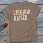 T-shirt with "VIRGINIA RAISED" text in beige on a taupe background.