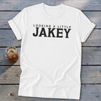 White t-shirt with black text "LOOKING A LITTLE JAKEY" on a wooden surface.