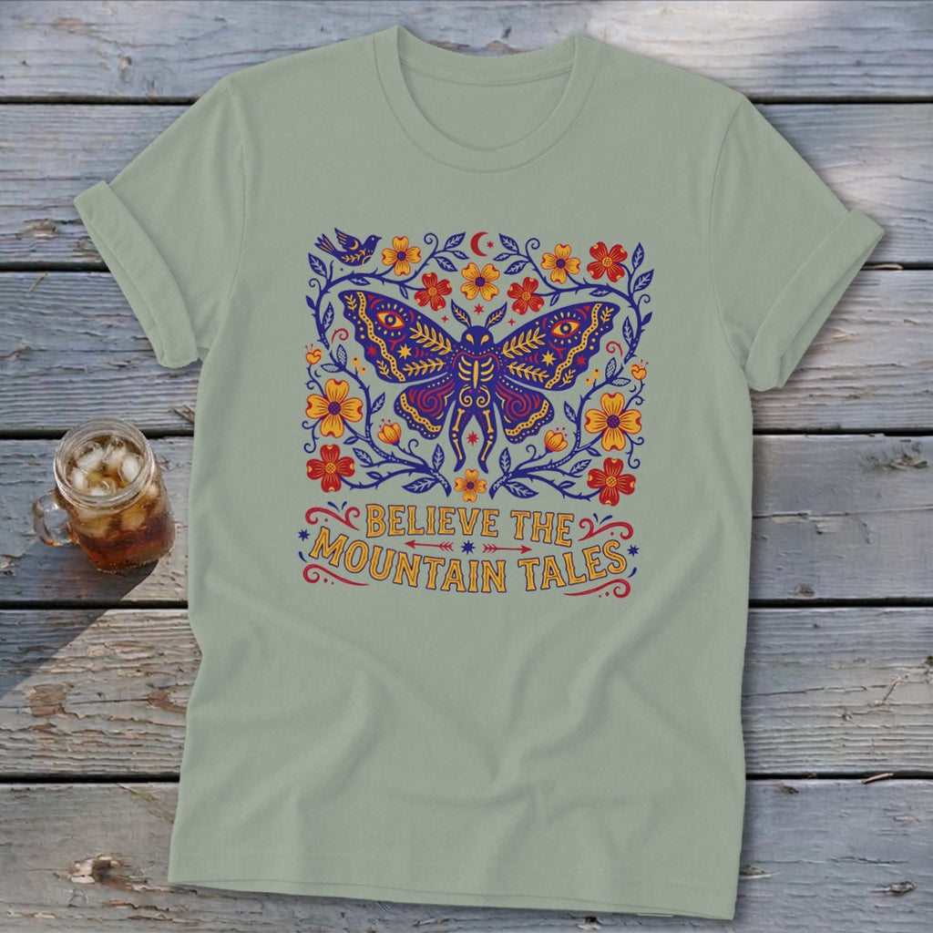 Light green t-shirt with a purple moth and floral design, text says "BELIEVE THE MOUNTAIN TALES".
