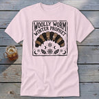 Light pink t-shirt featuring a black block-print graphic of a woolly worm with text reading Woolly Worm Winter Prophet.
