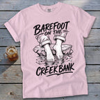 Pink t-shirt with "Barefoot On The Creek Bank" graphic and bare feet in water.