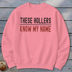 Pink crewneck sweatshirt with text "THESE HOLLERS KNOW MY NAME".