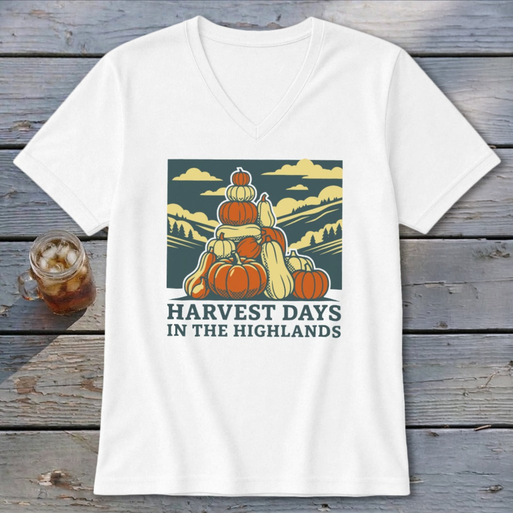 A white V-neck t-shirt featuring a graphic of stacked pumpkins with hills and sky and text reading HARVEST DAYS IN THE HIGHLANDS.