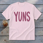 Pink t-shirt with "YUNS" in a dark pink font, next to a glass of iced tea.