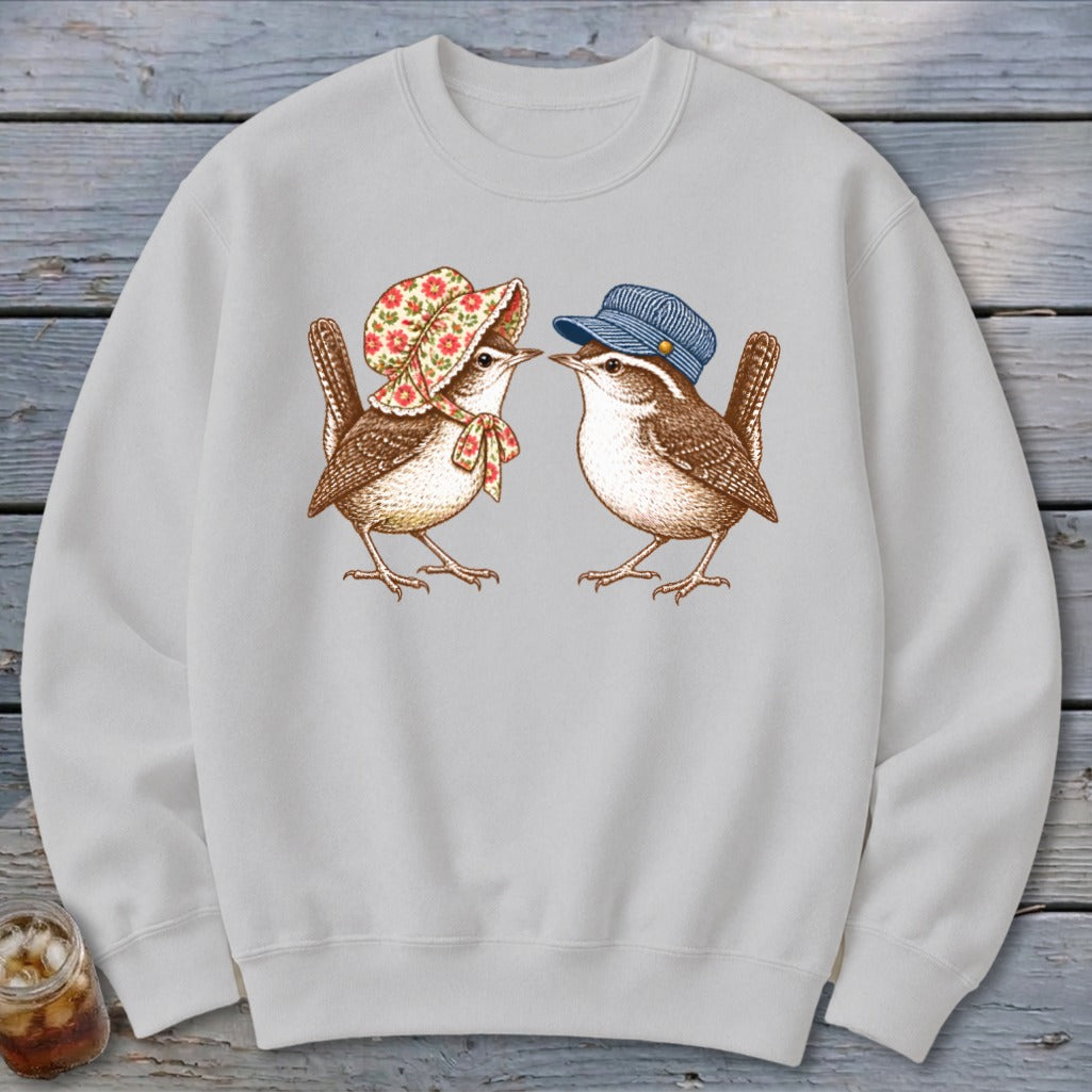 Two wrens wearing hats face each other on a gray sweatshirt.