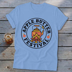 Light blue t-shirt with a circular graphic featuring a kettle over a campfire and text "Apple Butter Festival".